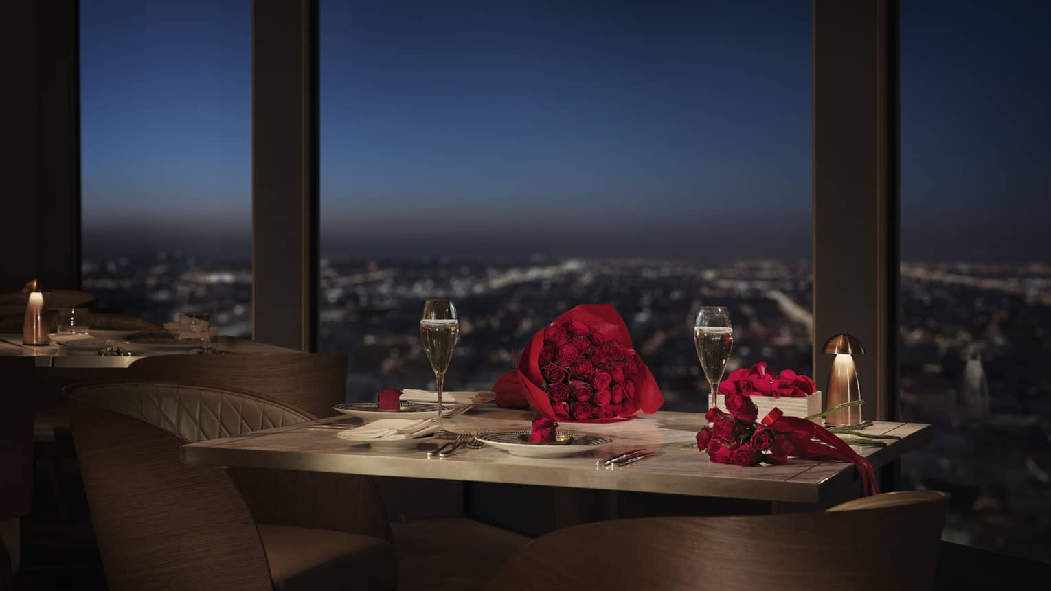 Red roses on small dining table by window overlooking city lights below