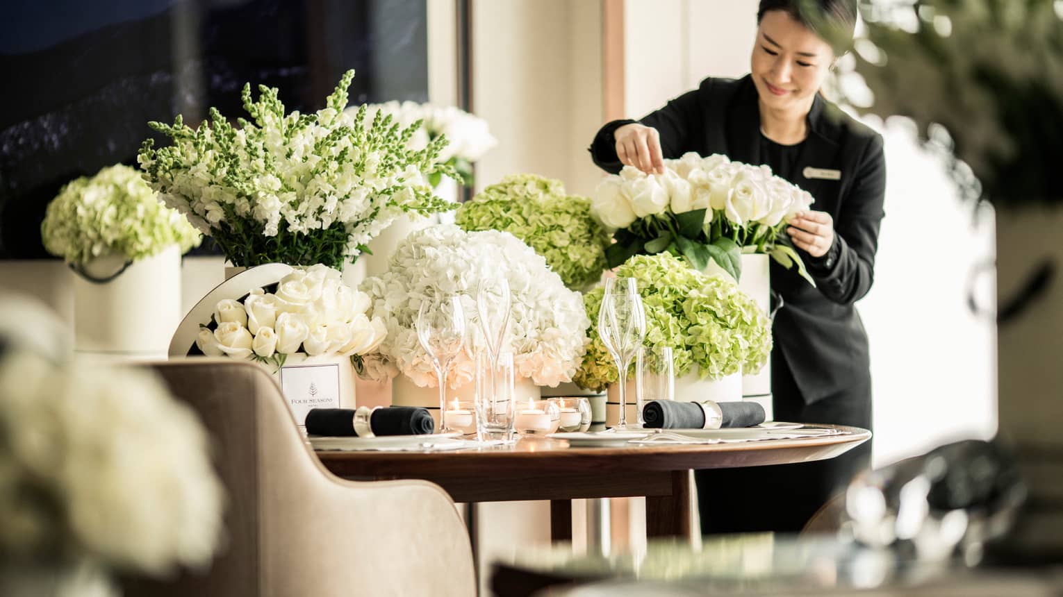 Hotel staff arranges white roses in vase on table with large vases, white flowers