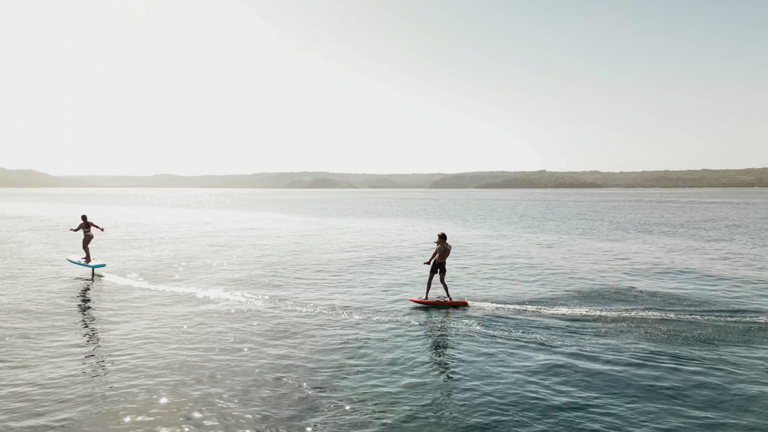 Two silhouetted figues riding e-foil surfboards in the water
