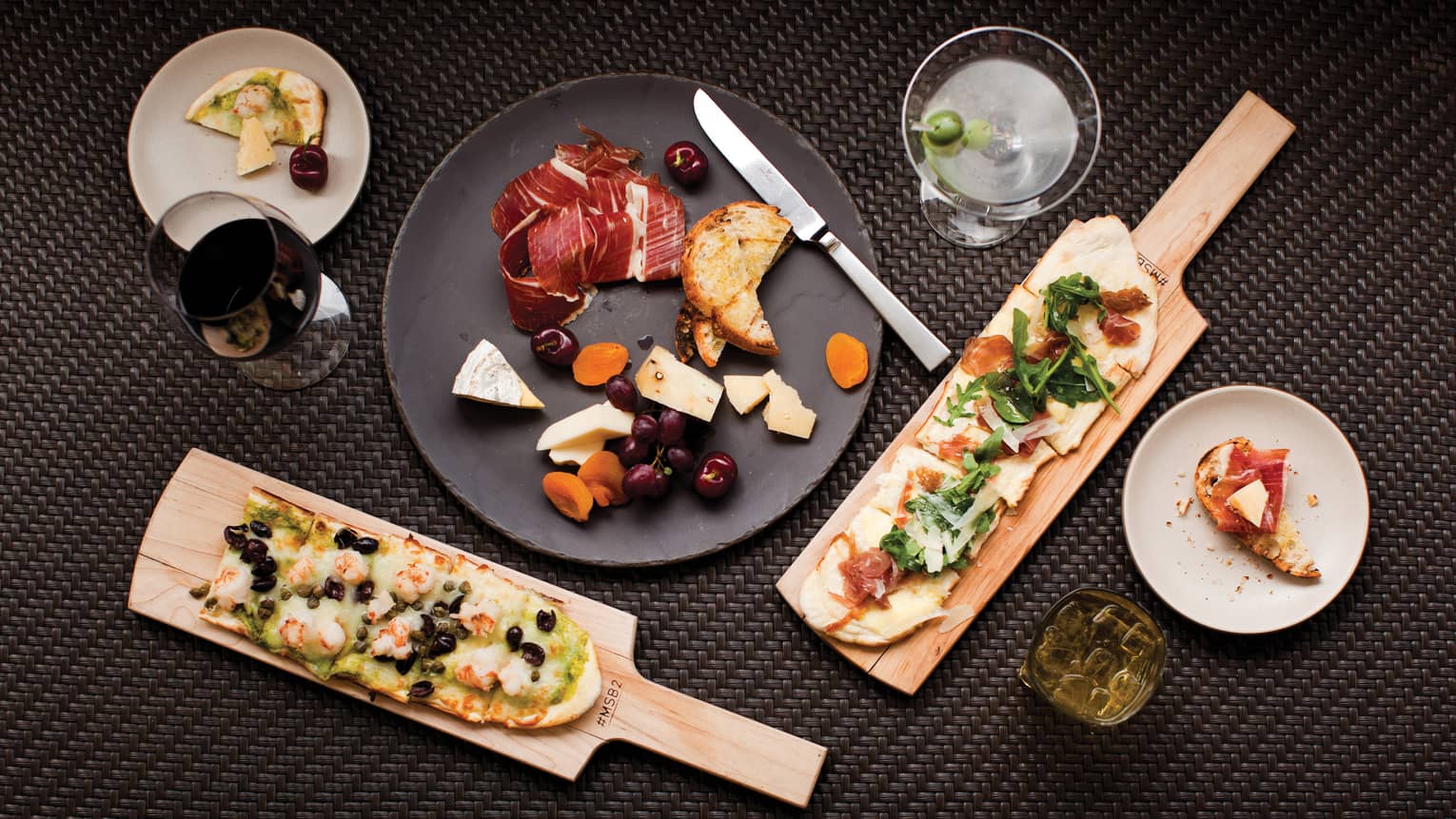 Aerial view of table with charcuterie and cheese platter, flatbreads on wood paddles, cocktails