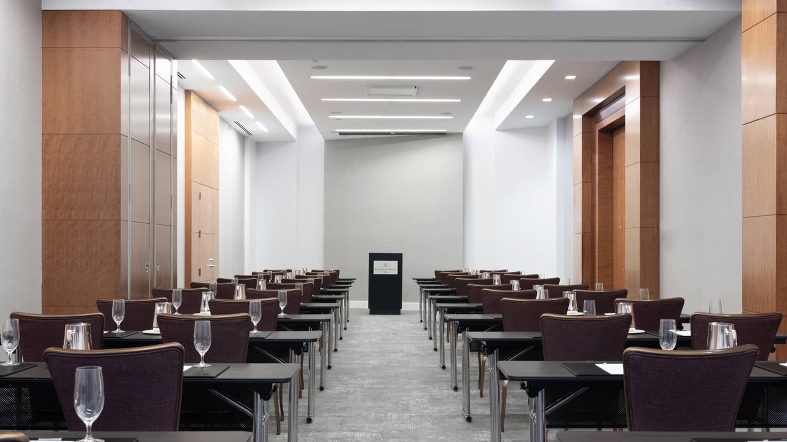 Rows of desks and chairs facing a podium on the other side of a long room.