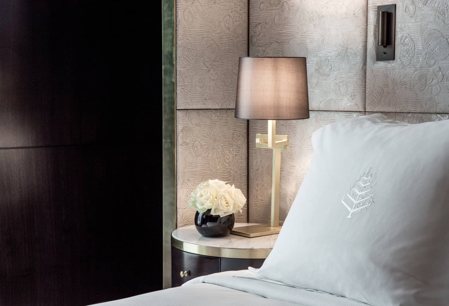 Premier room, close-up of pillow with Four Seasons logo, white roses in round black vase and bedside reading lamp
