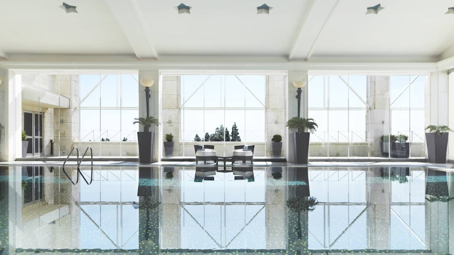 Indoor swimming pool reflecting light of three tall windows, white walls and pool chairs 