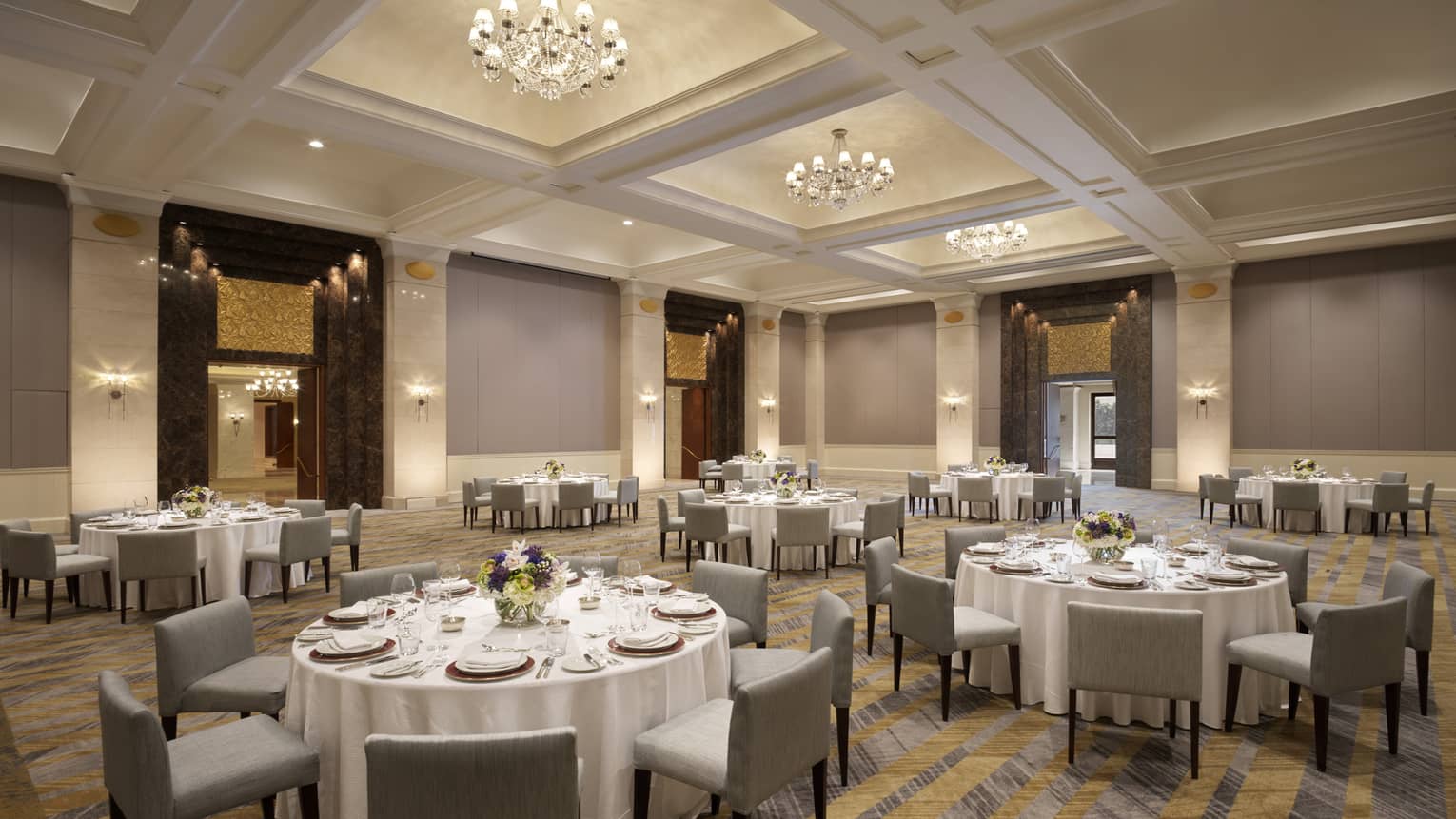 Several round tables set with white table clothes and square chairs.