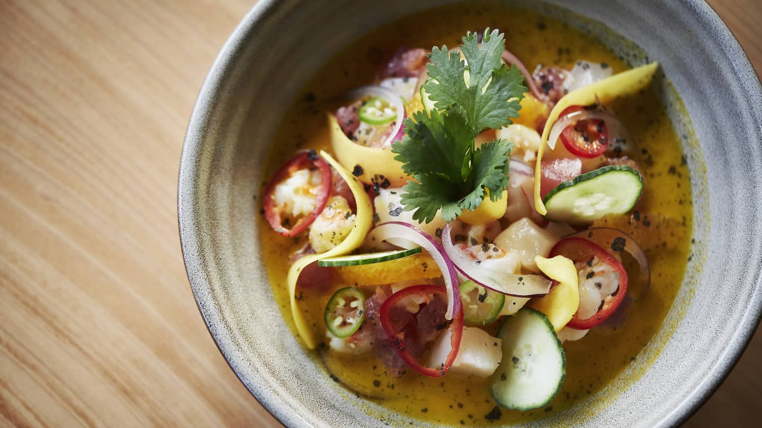 A gray ceramic bowl of a vegetable, curry soup garnished with cilantro and jalapenos 