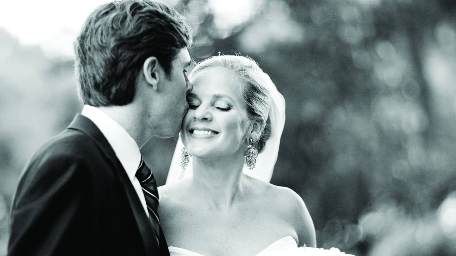 Black and white image of groom kissing smiling bride's cheek