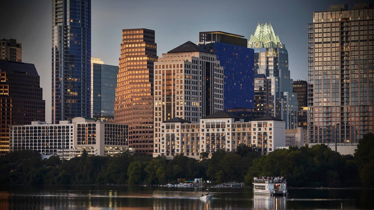 Buildings, trees, small ferry boat on water along Lady Bird Lake Austin waterfront