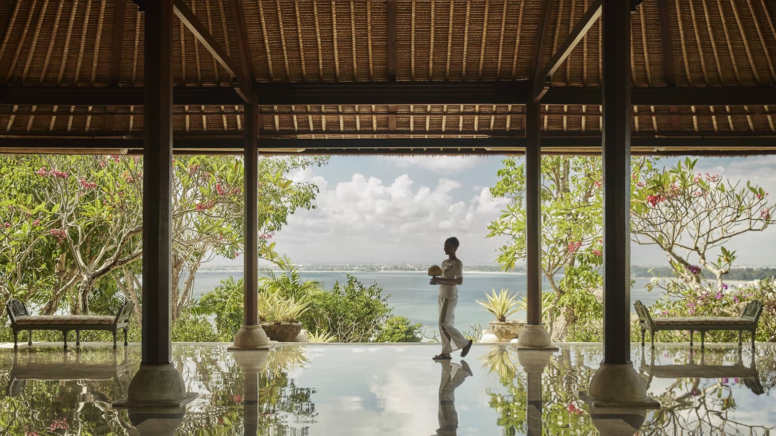 Hotel staff carrying flowers reflected onto floor of open-air pavilion