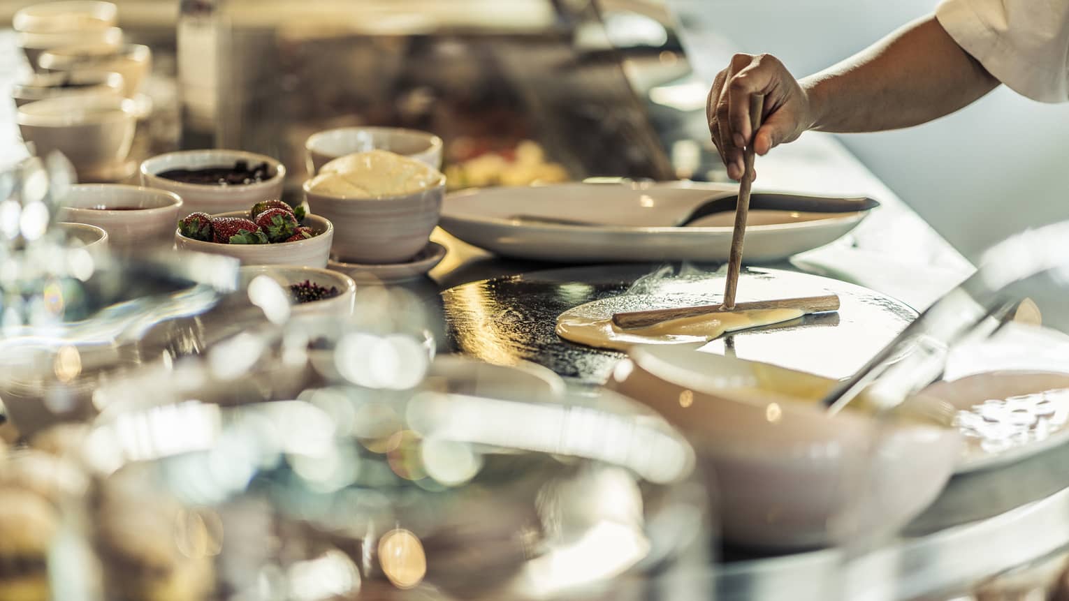 A chef pours crepe batter onto a hot plate near the crepe buffet