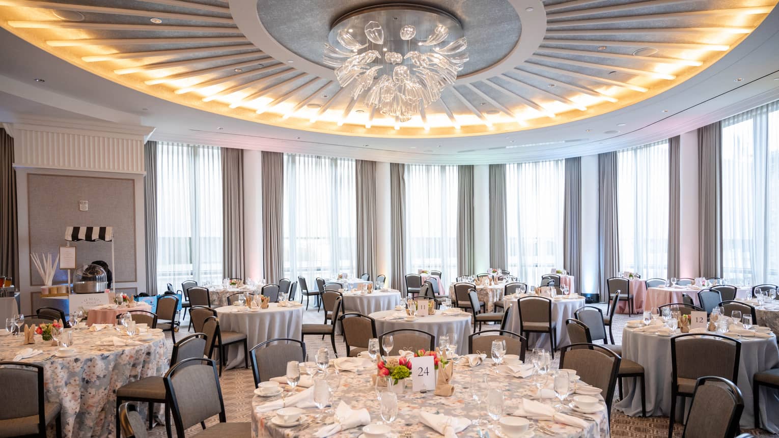 A ballroom with a chandelier and tables set with plates, napkins and glasses