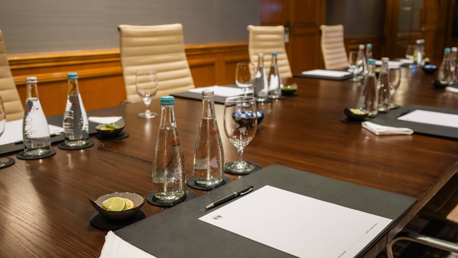 A meeting room with a table set with pens, paper, water and glasses