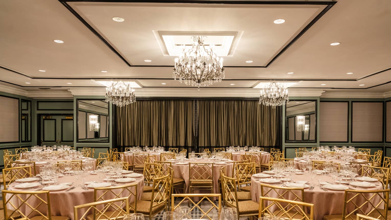 A room with chandeliers and round tables set with glasses and plates