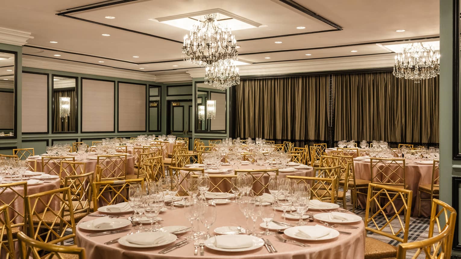 A room with green accents on the walls, round tables and chandeliers