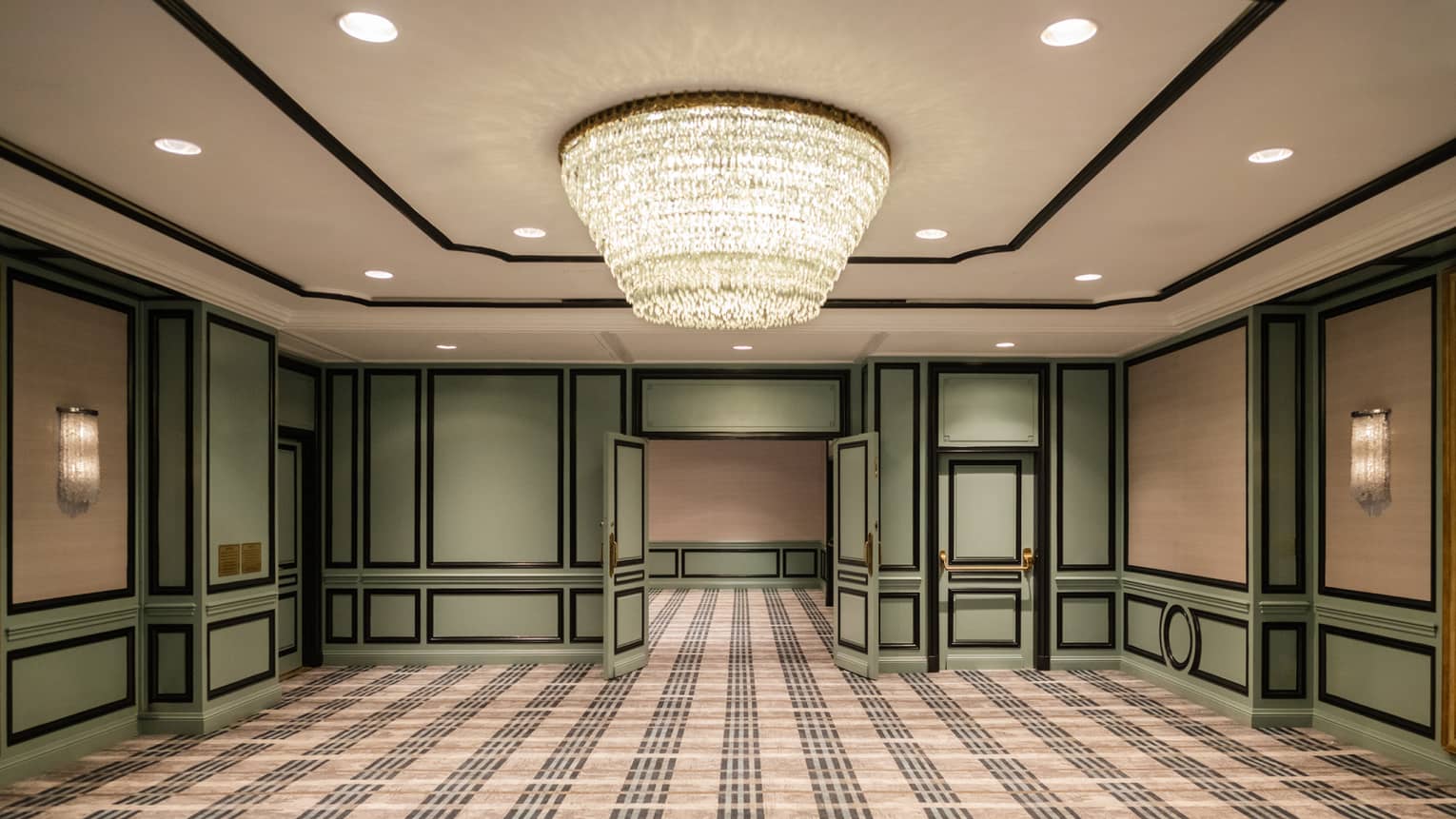 A room with green accents on the walls, green double doors and a chandelier