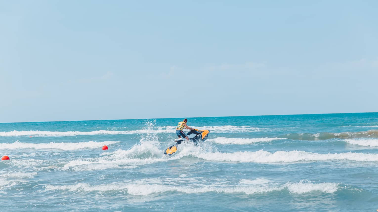 Person riding jet ski along waves in blue ocean