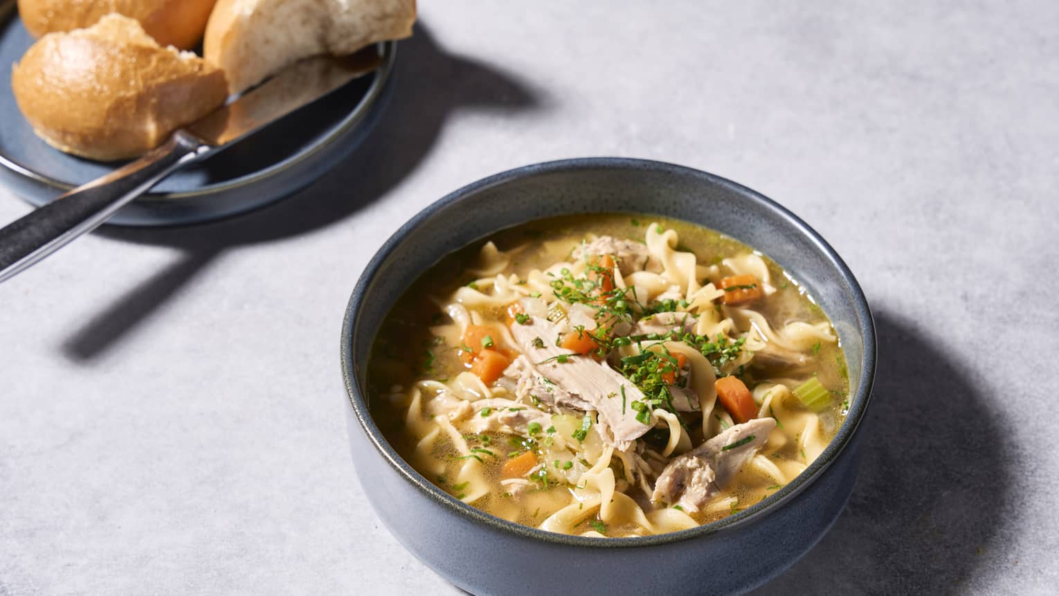 Chicken noodle soup with seasoning and bread slices on the side.