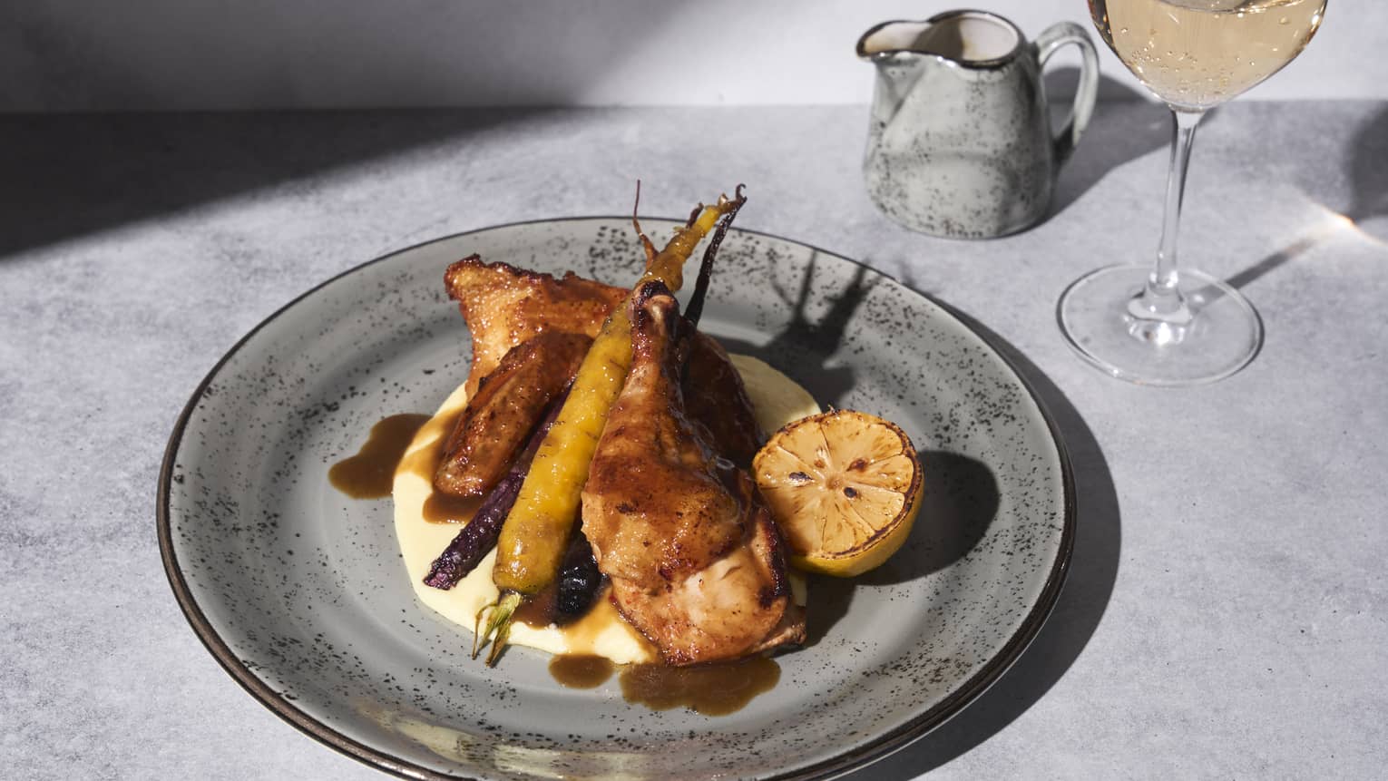 Chicken with potatoes and a lemon slice and wine glass on the side.