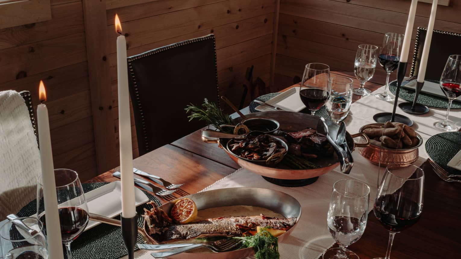 A dining table set with multiple dishes, glasses and candles