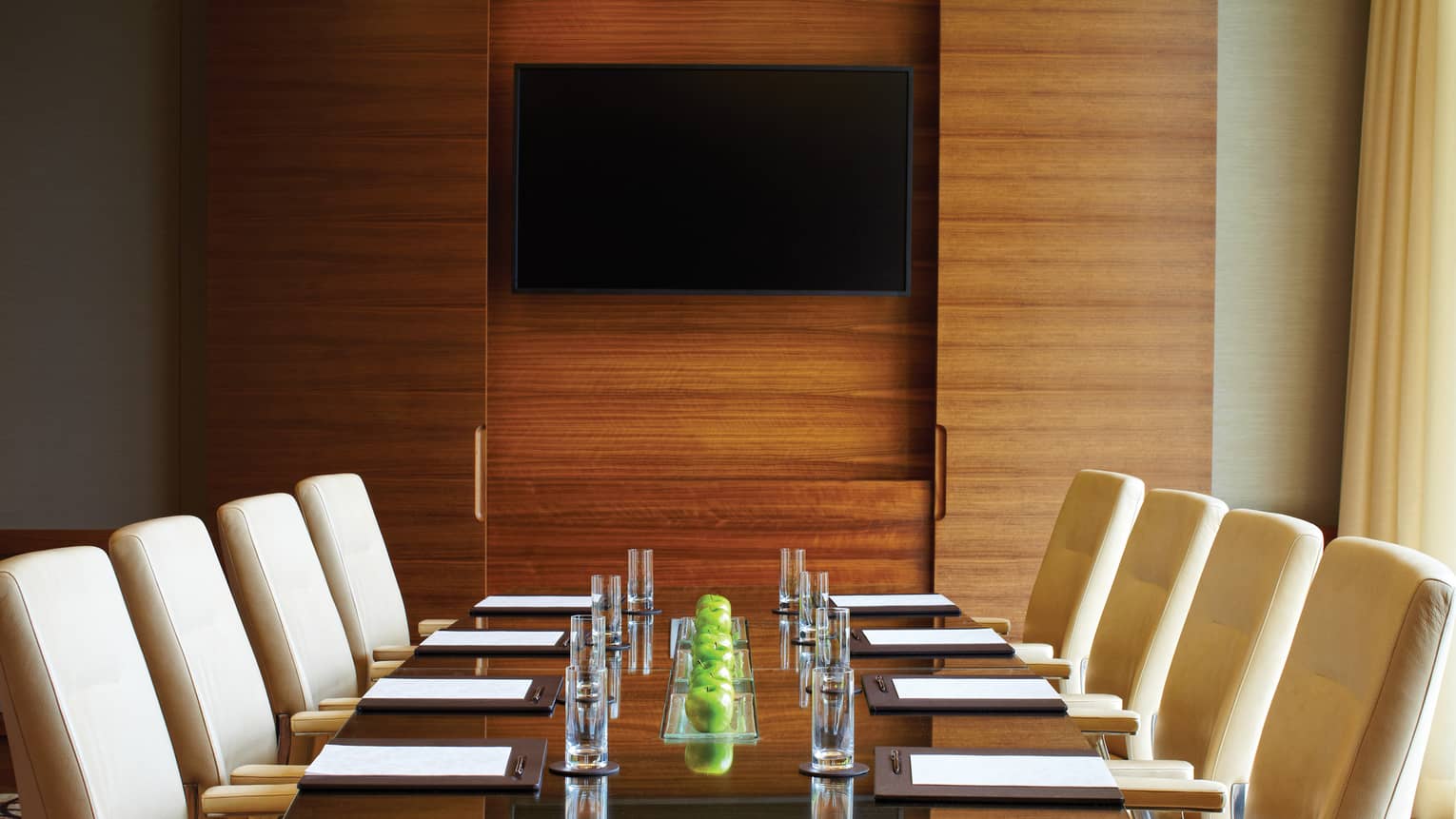 Boardroom meeting table set with green apples, water glasses and lined with white leather chairs 
