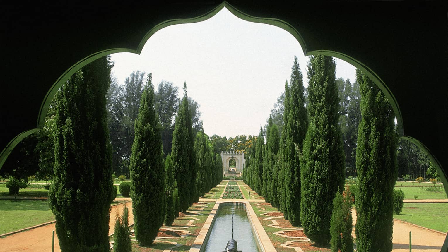 Thin trees line a strip of water and flowers in Tipu Sultan's Gardens