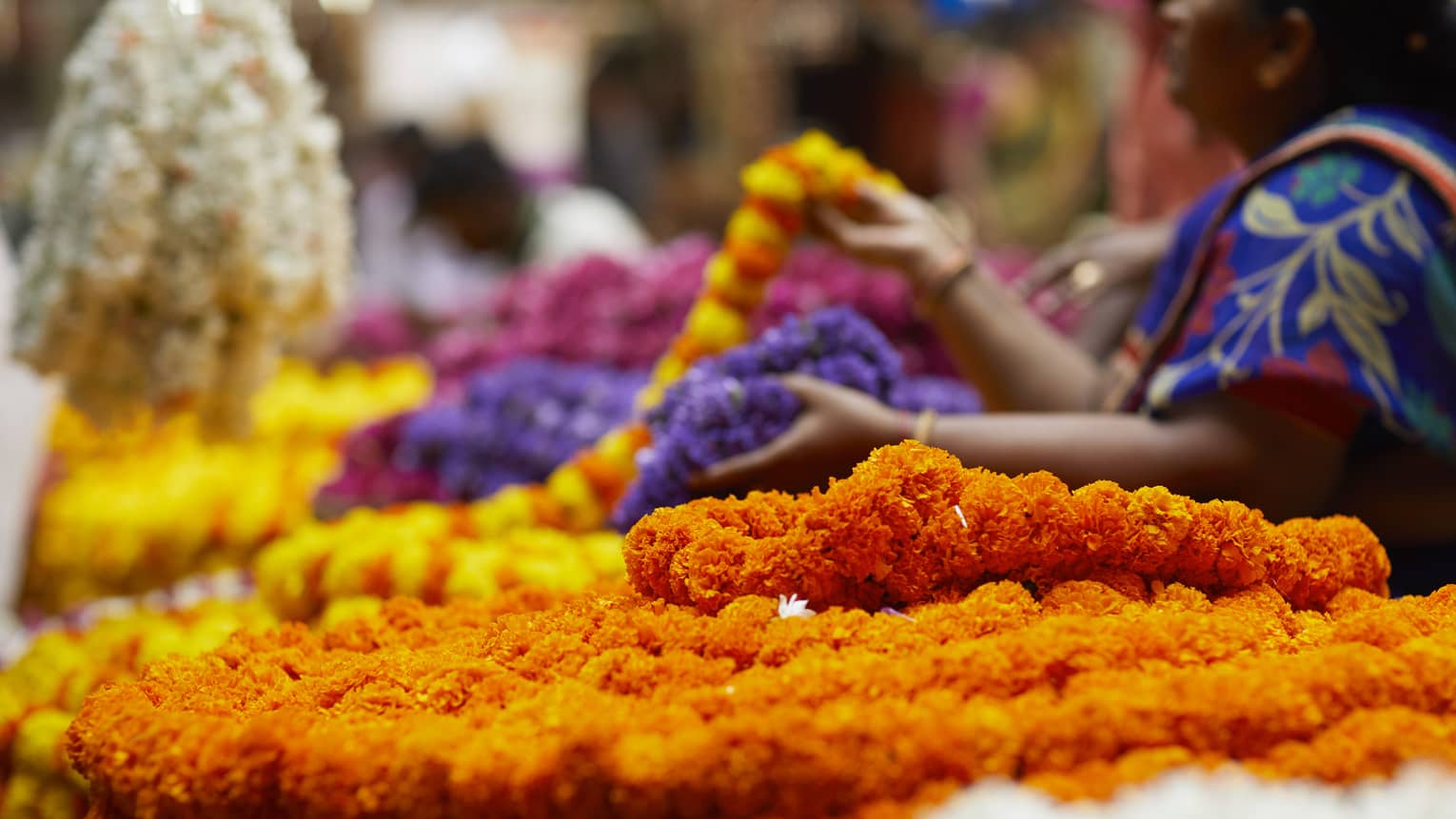 Close-up of vibrant chains of flowers amid a bustling market scene, where people sell and browse colourful floral displays.