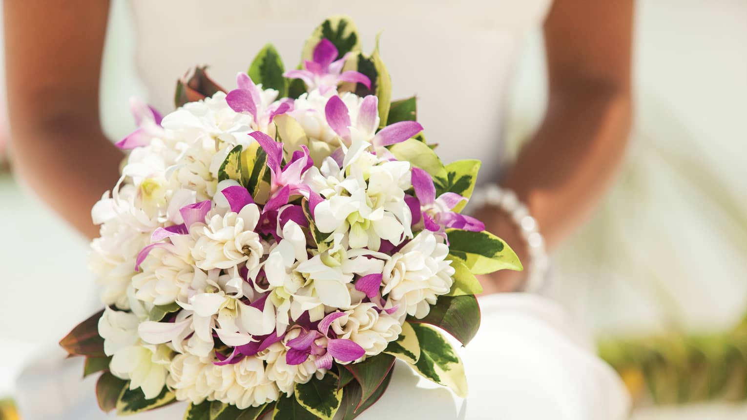 Close-up of bride holding wedding bouquet with purple and white flowers