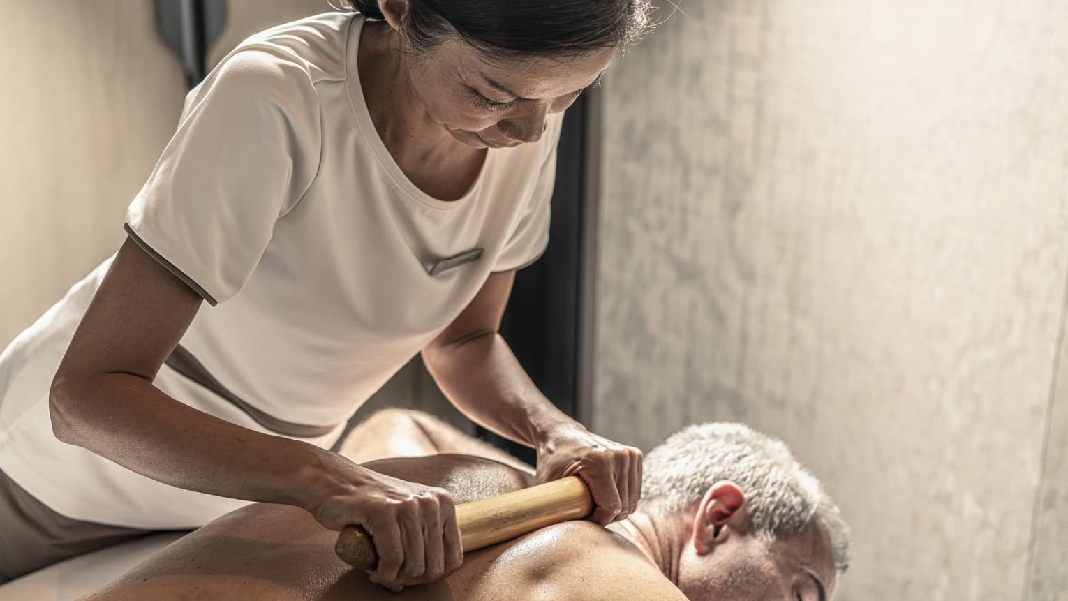 Massage therapist performs a bamboo massage on male guest