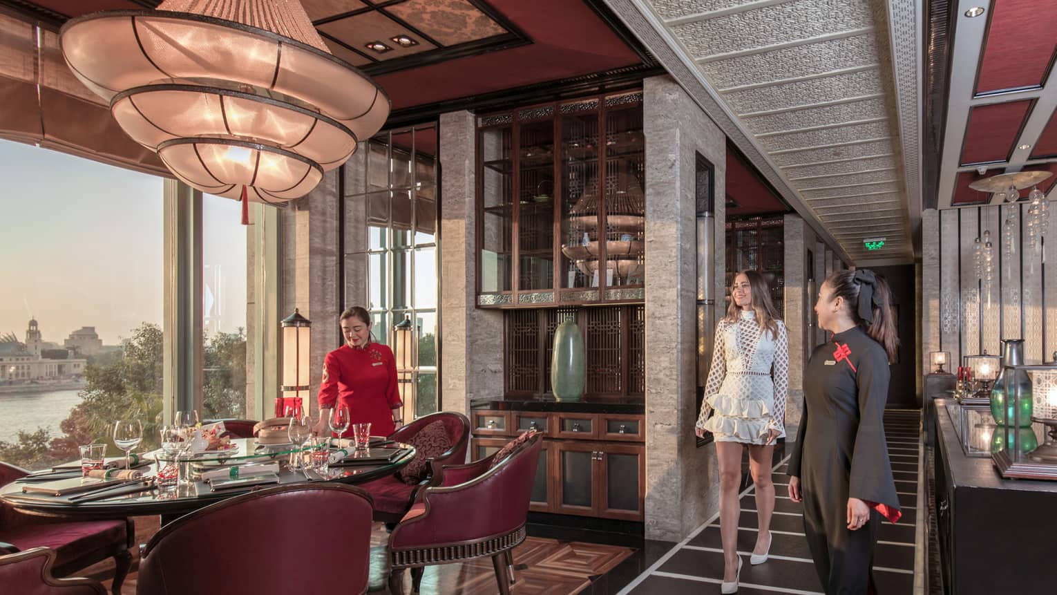 A guest is shown to her table, surrounded by burgundy chairs, in a luxurious restaurant with opulent decorations. 