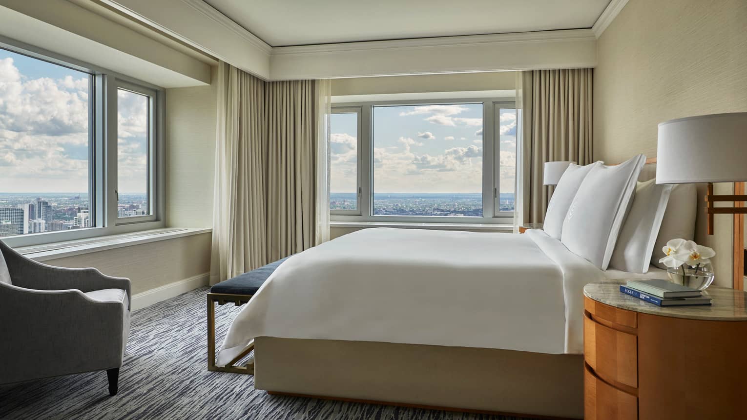 City-View corner suite bed with blue velvet bench, grey armchair, large windows with city views