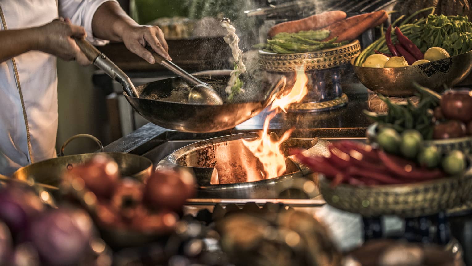 Close-up of chef stirring meals in copper pans over stove, flames 