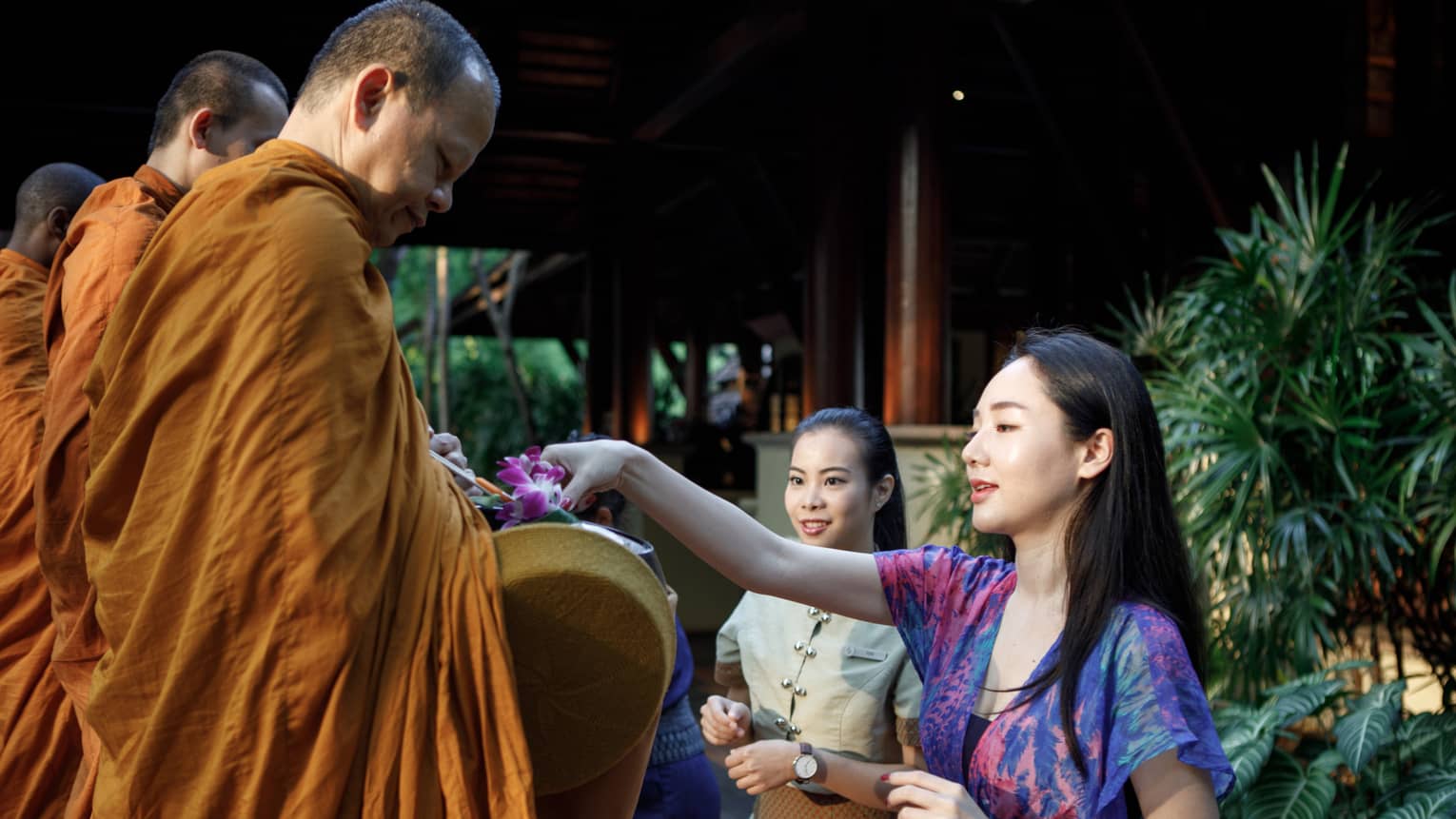 A woman giving an offering to a monk in an orange robe.