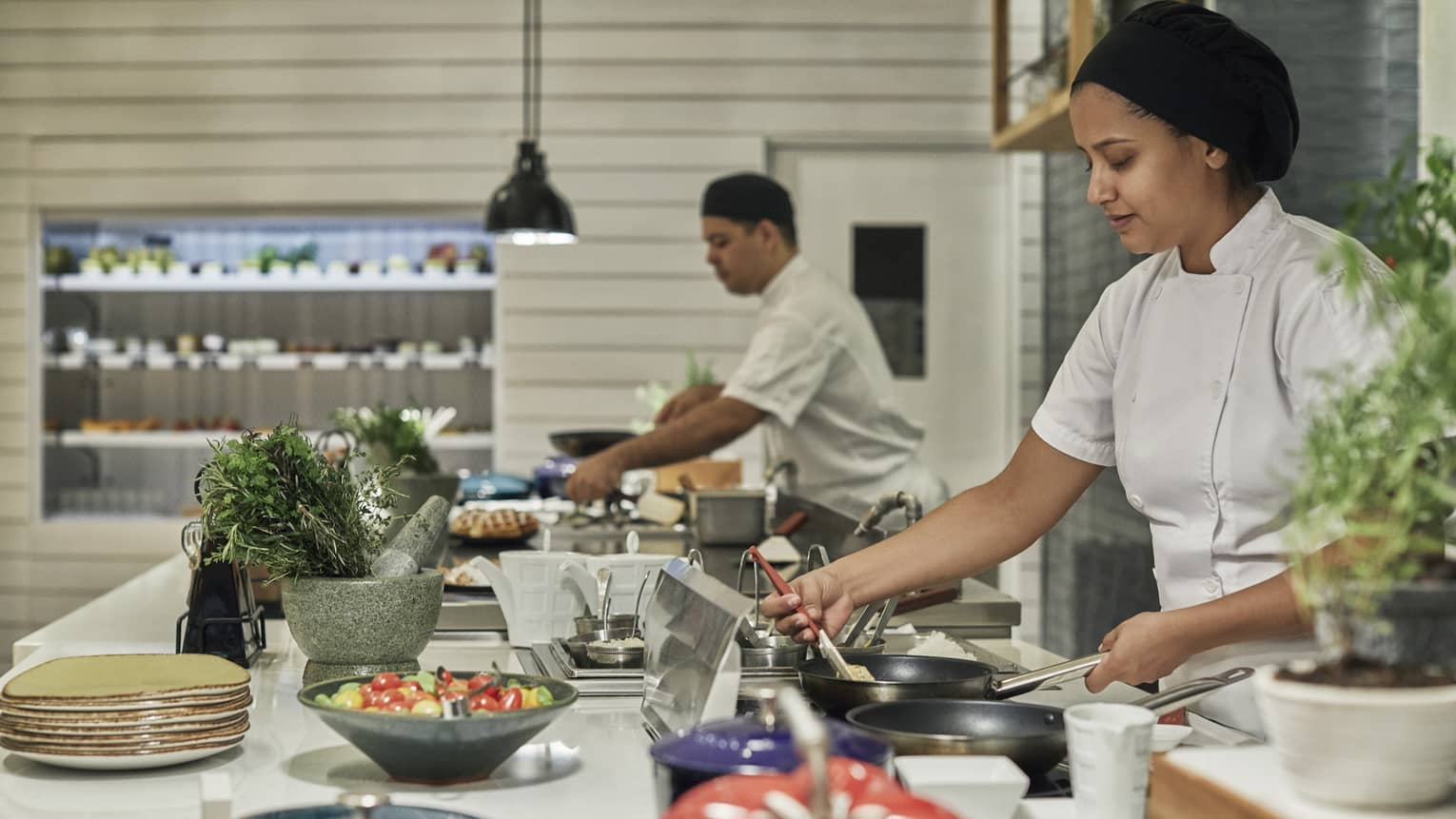Two chefs prepare a dish of colorful vegetables on the island of a kitchen.
