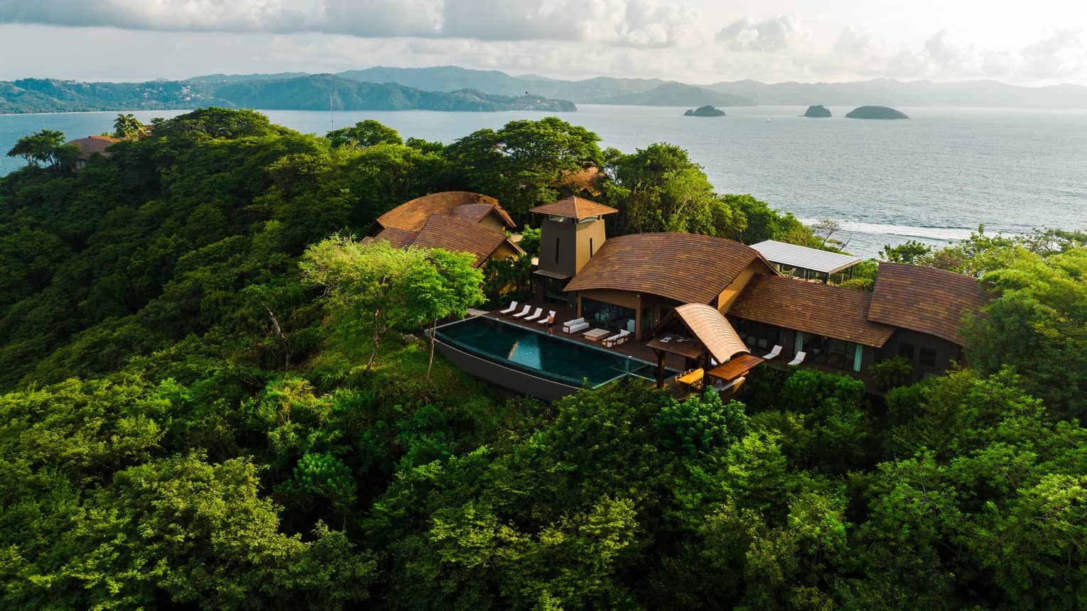 Villa tucked in a green hillside with the ocean in the background
