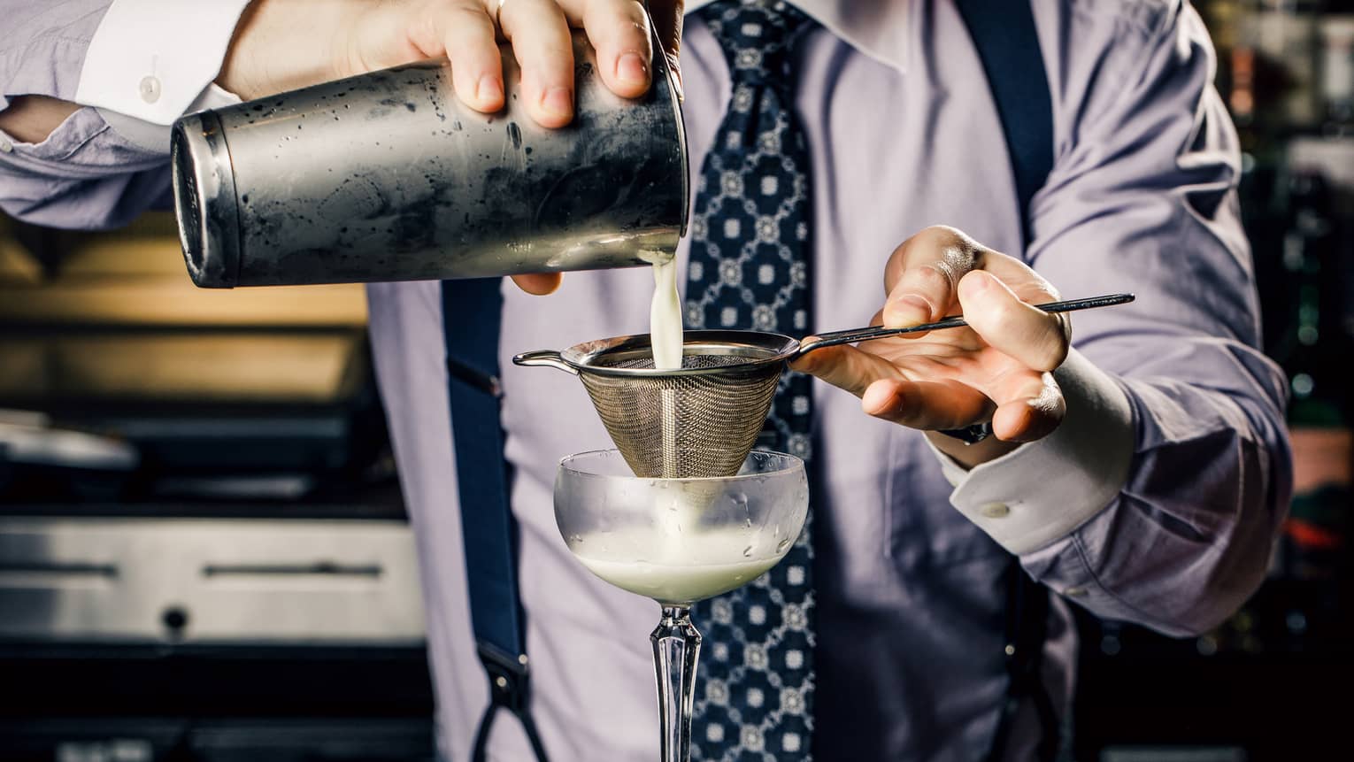 Churchill Club bartender wearing tie pours white cocktail through strainer into glass
