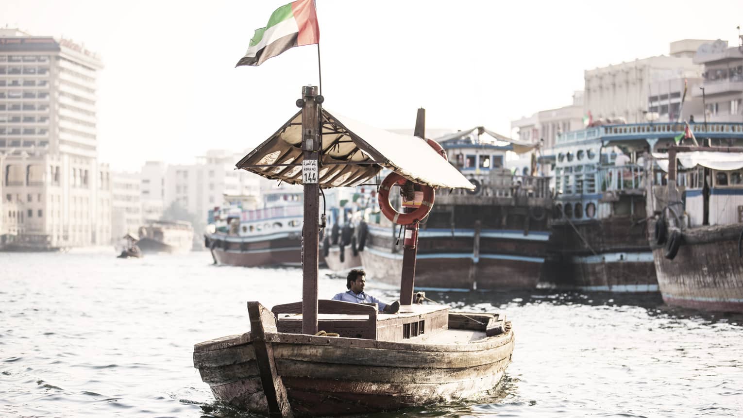 A small wooden boat flying the UAE flag as it sails down a small waterway. 