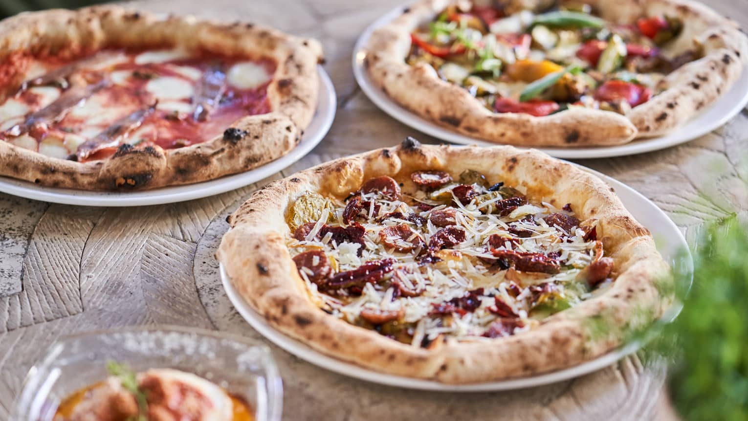 Three signature pizzas, each with unique, vibrant toppings