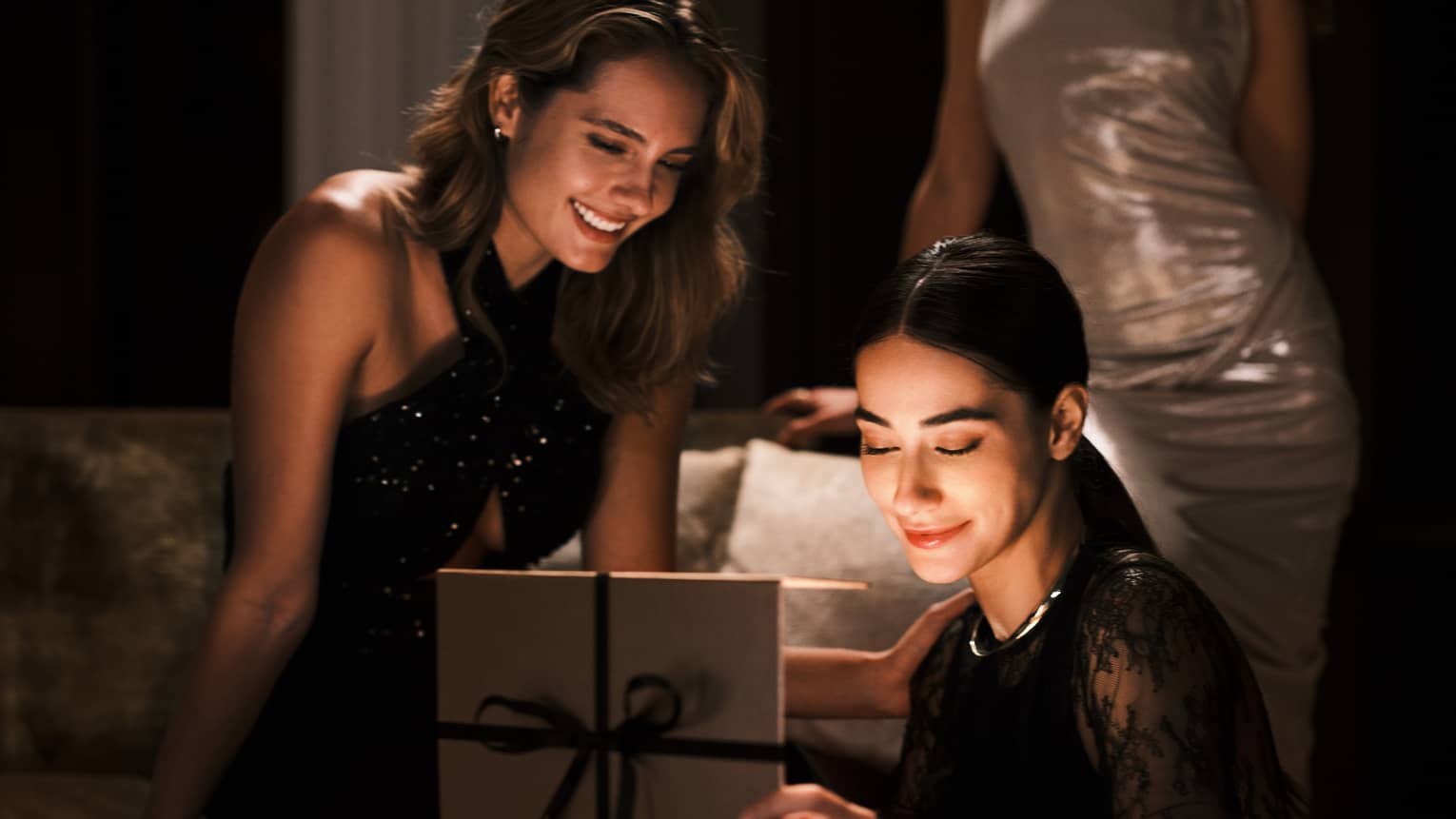 Two guests at a restaurant table smiling while opening a gift.