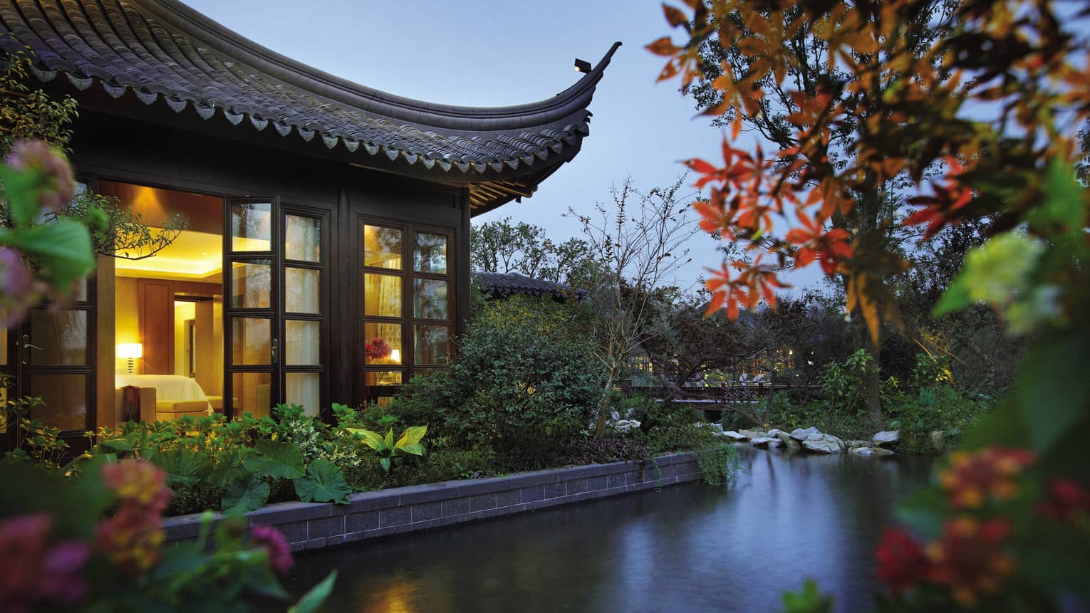 Side view of Lake Suite villa with sweeping roof, garden over water at night