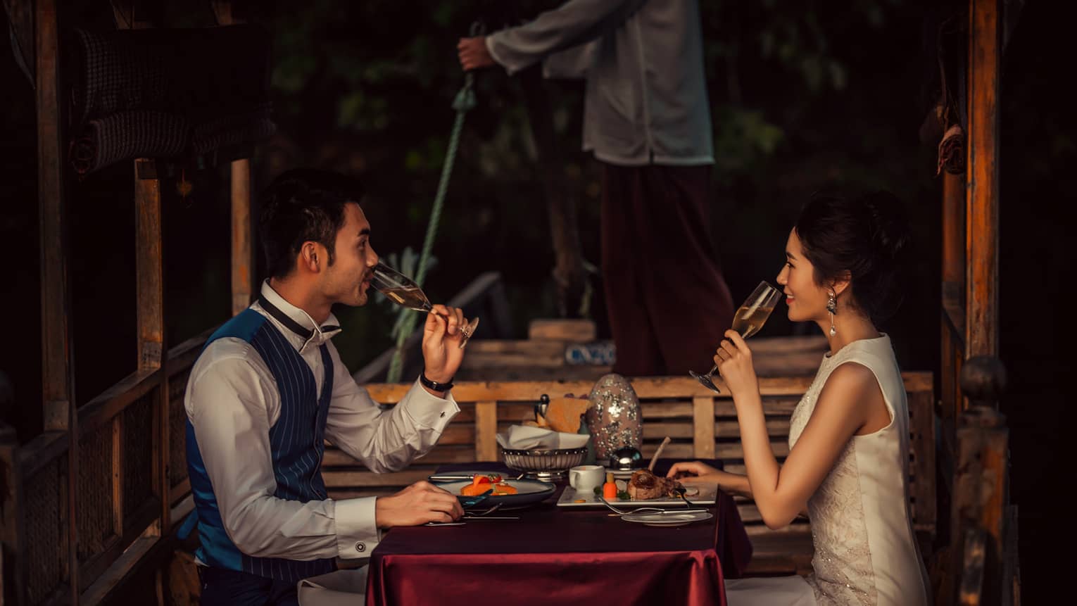 Couple sipping Champagne, dining at small table on traditional Chinese wooden boat