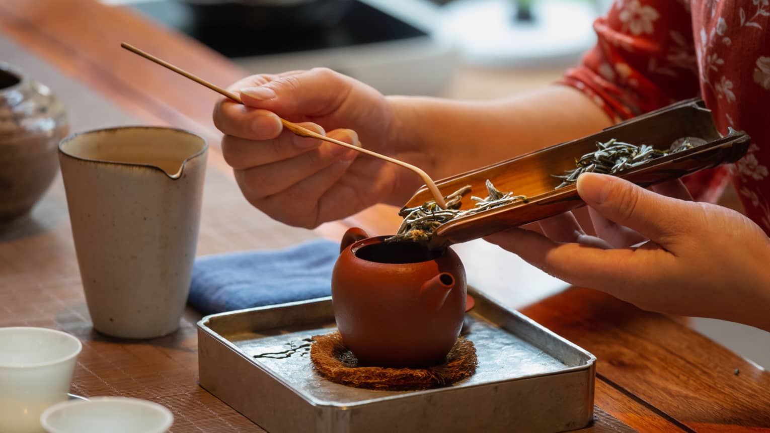 Woman scrapes loose tea leaves into small clay pot at Tea Plantation
