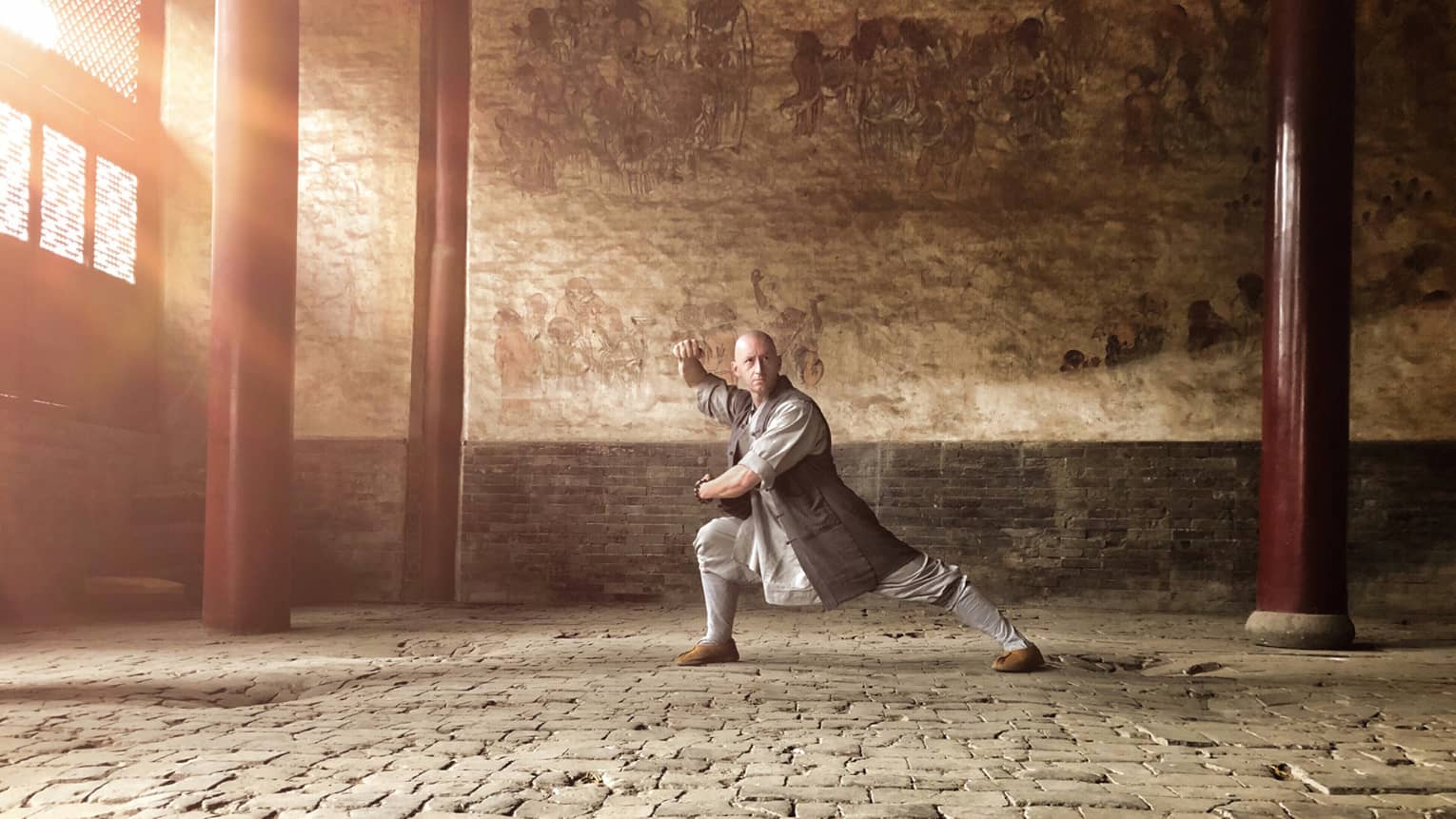 Man in grey attire practicing kung fu in a stone building