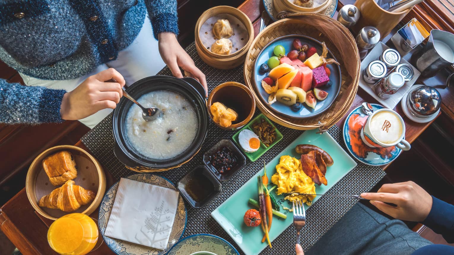 View from above as two guests savour a sumptuous array of vibrant dishes, including pastries, congee, fresh fruit and coffee.