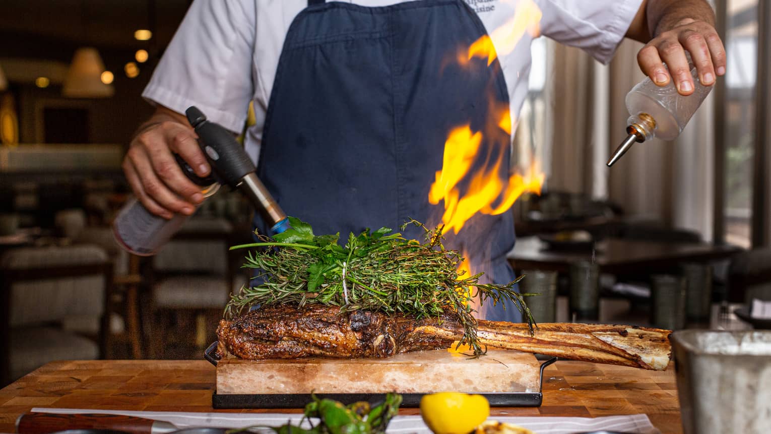 A chef using a blowtorch and oil to cook meat.