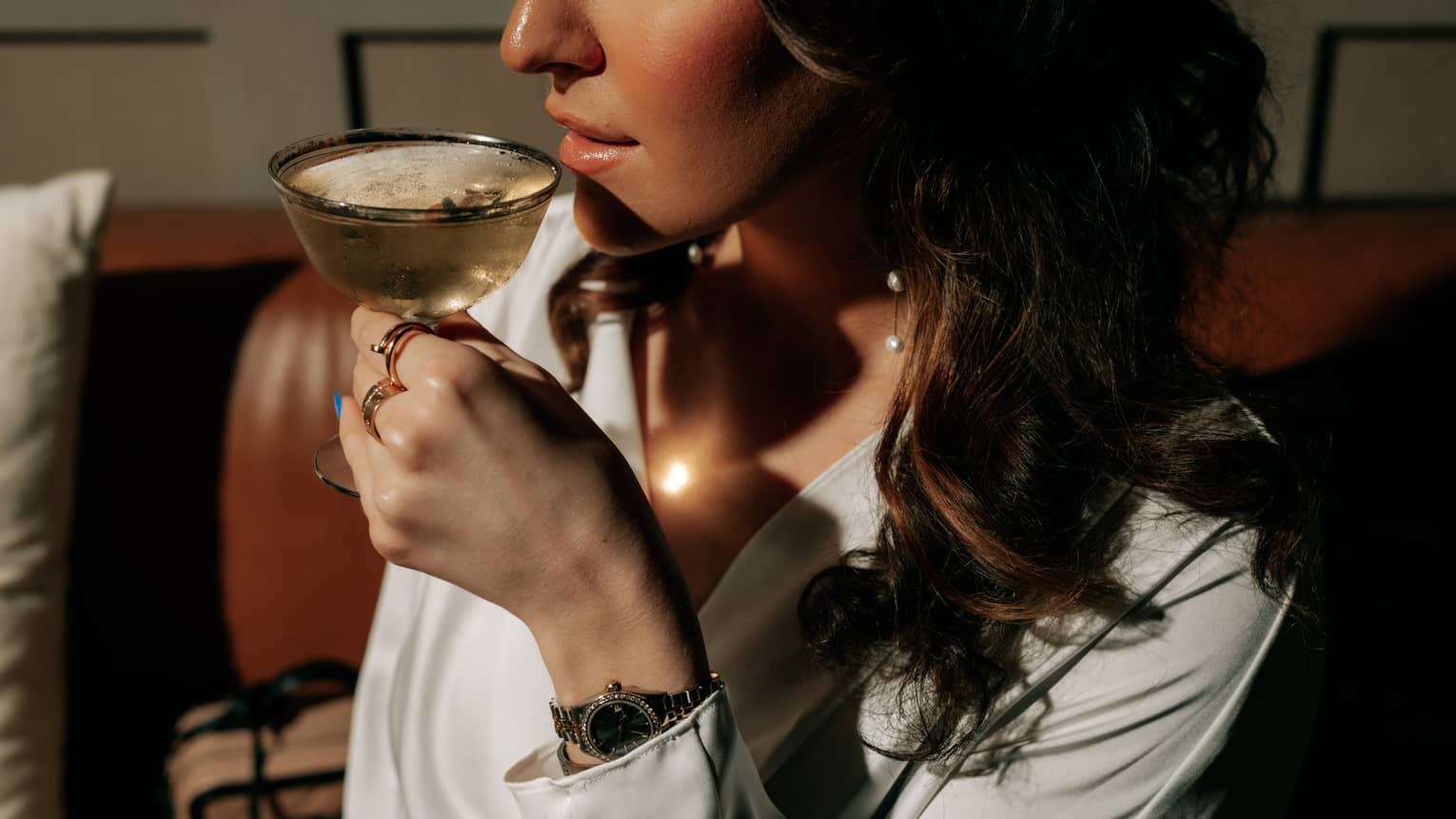 A woman with long, dark hair is about to sip a cocktail from a coupe glass.