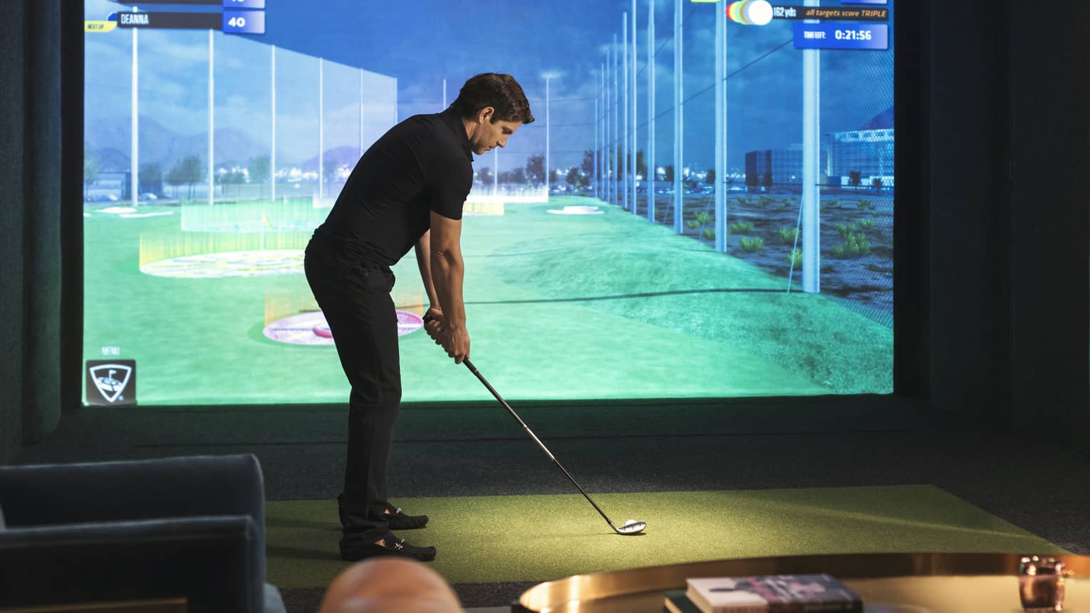Man with golf club stands in front of screen showing Virtual Fairway
