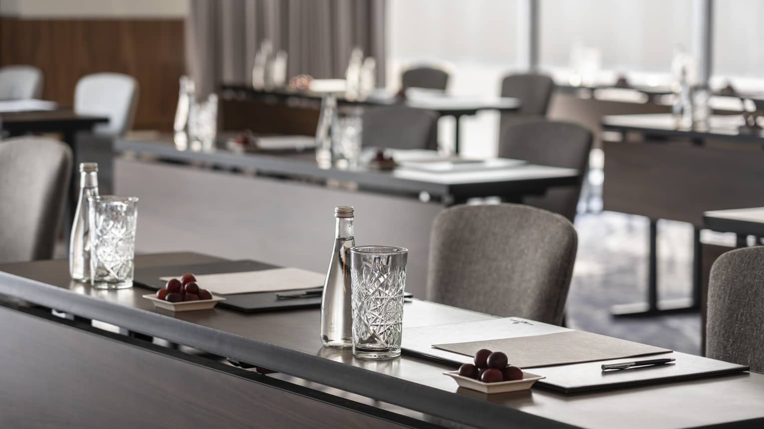 A close up of long desks with papers and water placed at each seat.