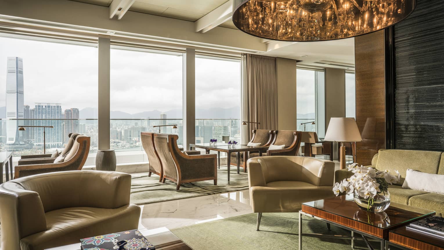 A spacious, modern lounge area with large windows offering a panoramic cityscape view. The room features comfortable armchairs, sofas, wooden furniture. 