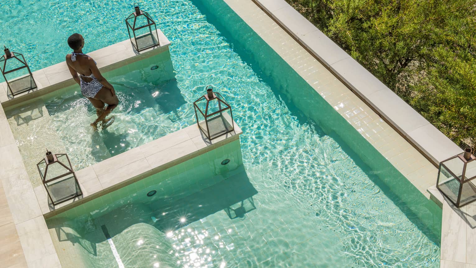 Aerial view of woman in swimsuit walking into plunge pool on sunny day