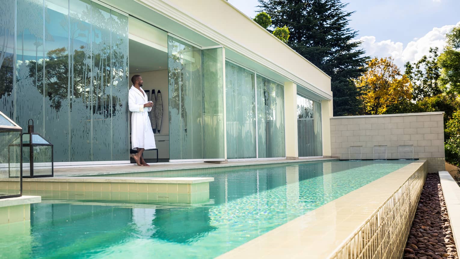 Man wearing bathrobe stands by glass wall over plunge pool