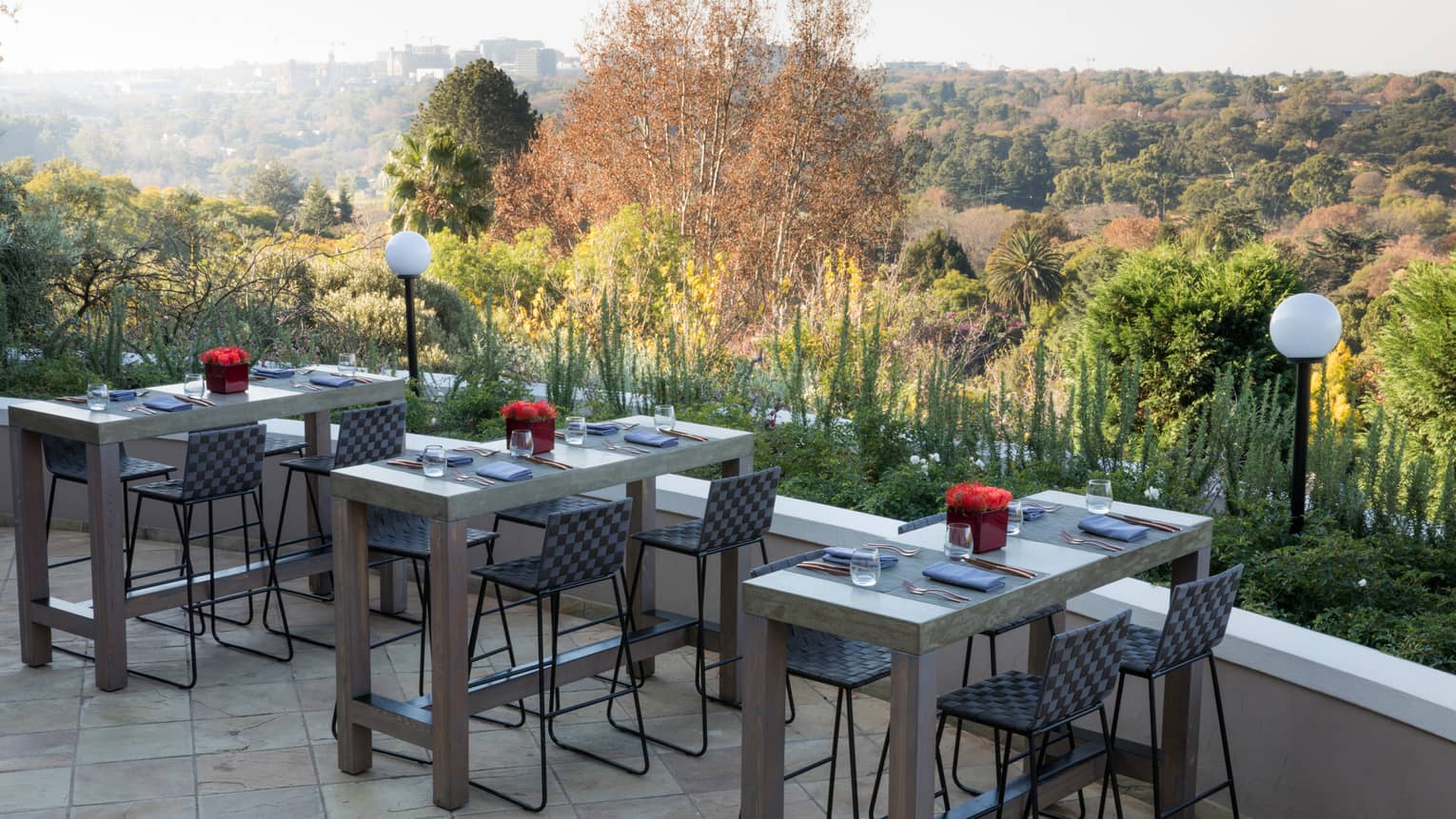 Stone terrace seating area with three set small rectangular tables over forest view